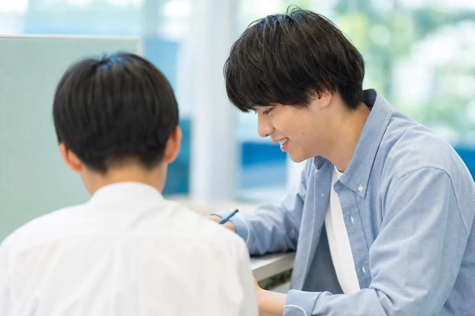 大学生になった卒業生講師が、後輩の生徒に笑顔で教えている場面（世代がつながる構図）