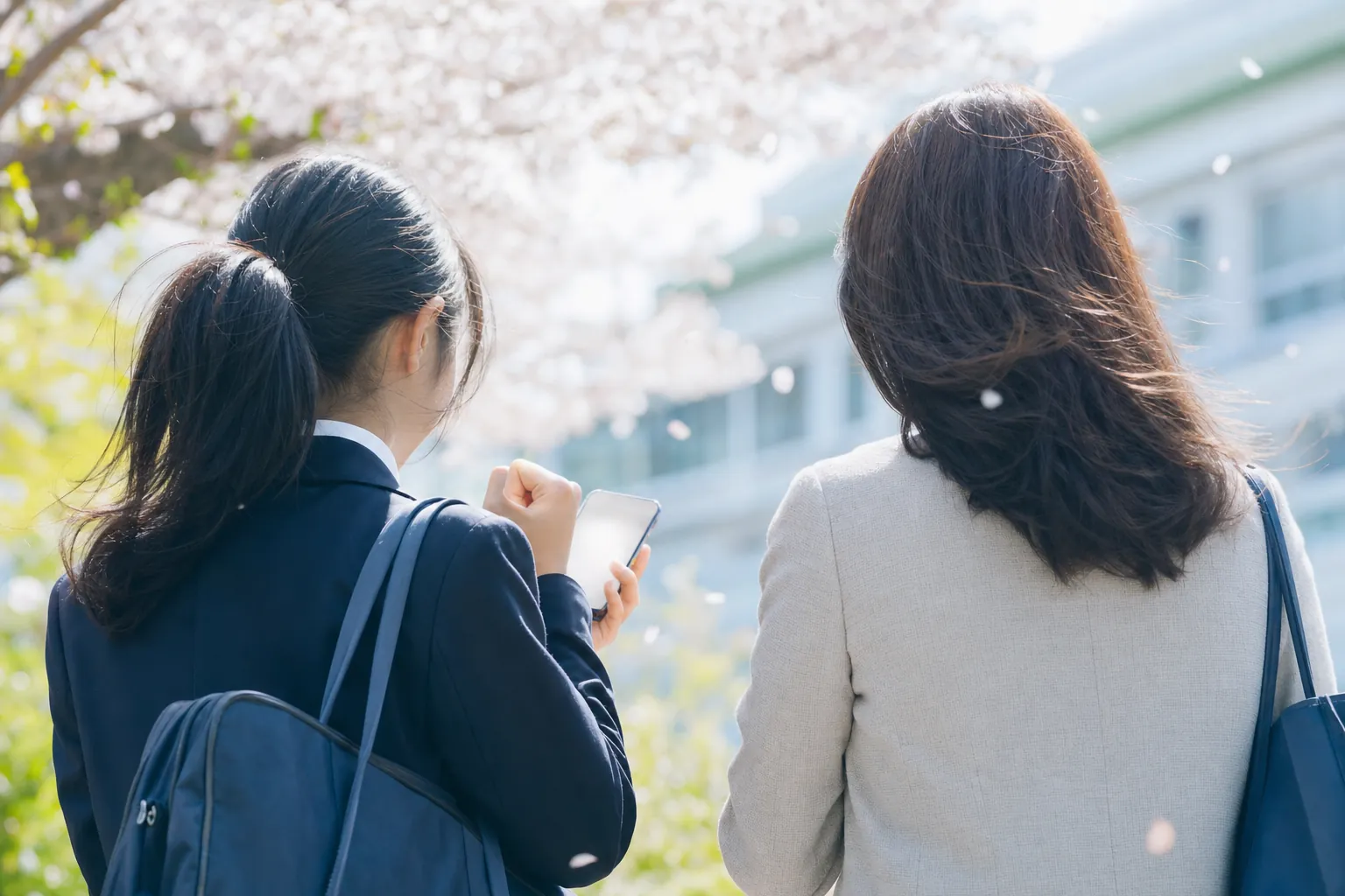 合格発表の日、スマホの合格画面を握りしめてガッツポーズする高校生の後ろ姿。隣に寄り添う母親の後ろ姿。春の光